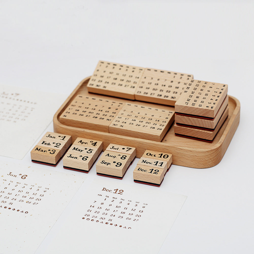 A crisp stamped December calendar grid on paper, displayed next to the complete 20-piece vintage wooden perpetual calendar stamp set resting in its custom wooden storage tray.