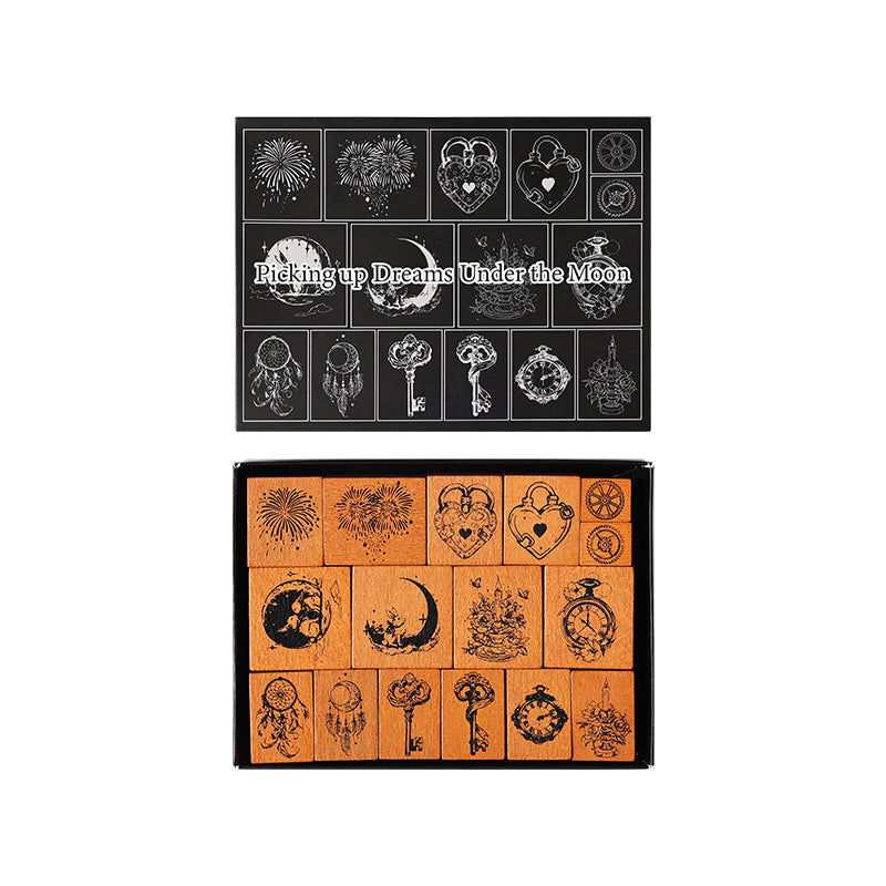 A clean studio product shot on a pure white background showing the complete Dreams Under the Moon 16-piece wooden stamp set. The elegant black display box stands upright on the left, with all sixteen uniquely shaped stamps arranged neatly next to it in a grid.