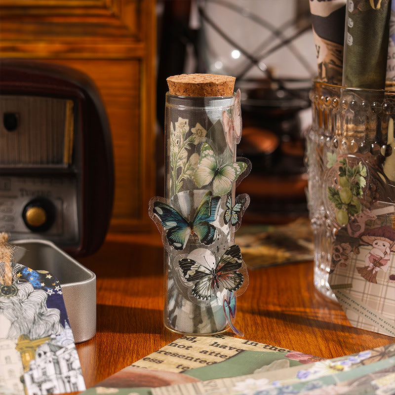 Translucent vintage butterfly stickers elegantly applied to a small glass vial with a cork stopper, showcasing creative DIY craft ideas using our scrapbook supplies.
