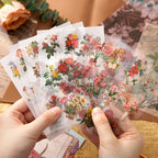 Hands holding up several sheets of translucent PET floral stickers from the Letter From Flowers kit. The high-quality botanical rose and wildflower designs are slightly see-through, ideal for seamless scrapbook layering.