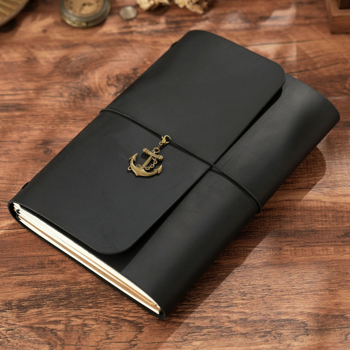 Trifold A5 black leather notebook with brass anchor charm on wooden desk