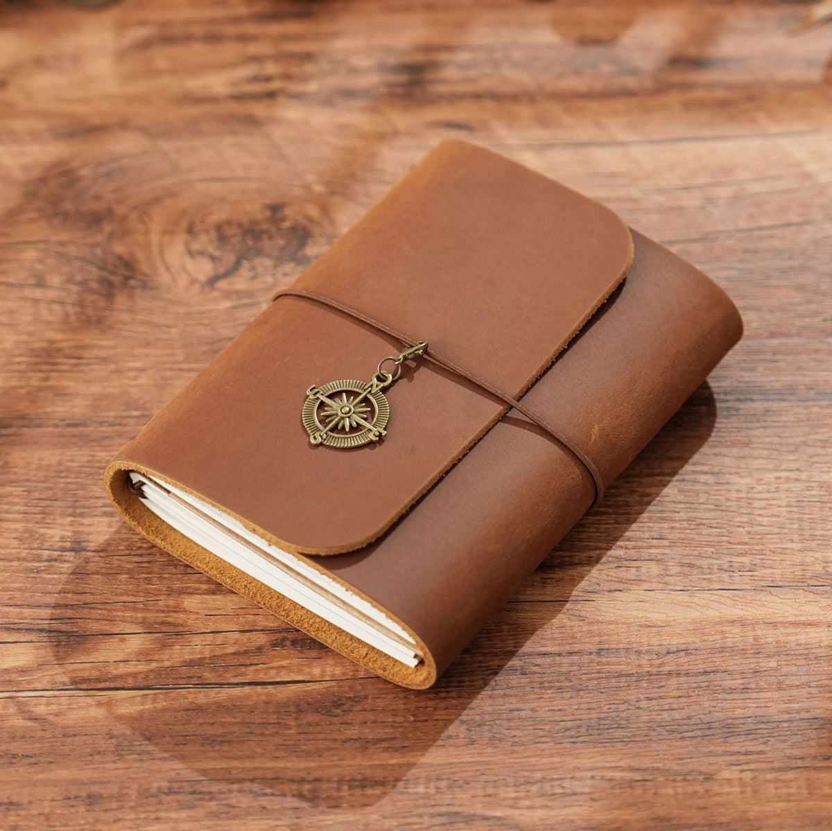 Brown trifold leather journal wrapped with elastic cord and brass charm