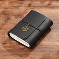 Trifold dark green leather notebook with brass compass charm on wooden desk