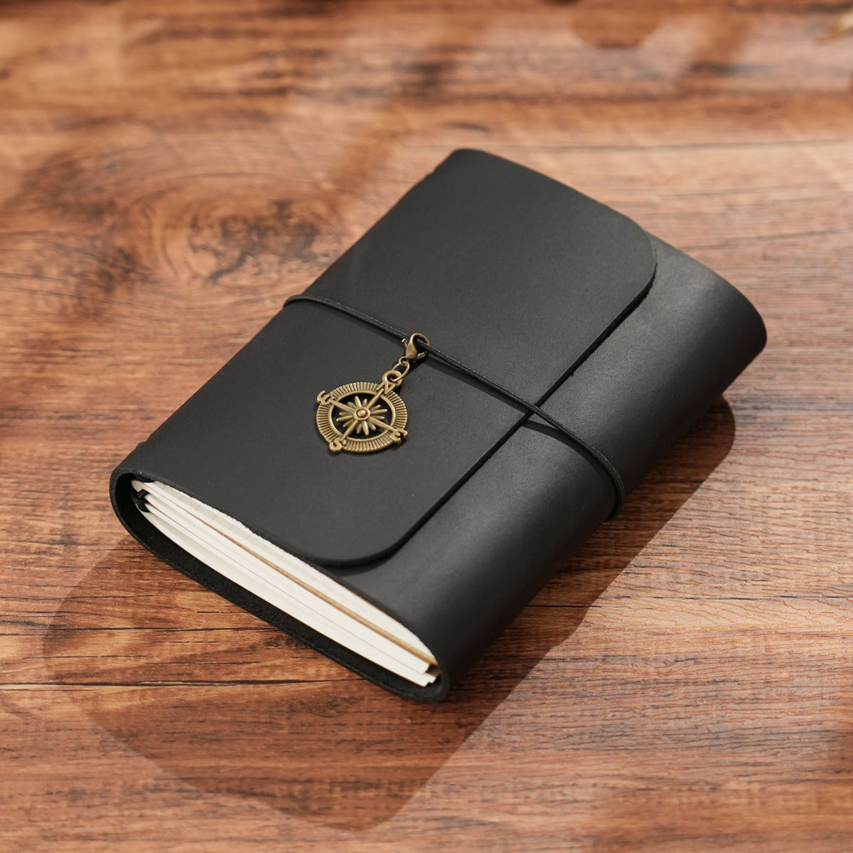 Trifold dark green leather notebook with brass compass charm on wooden desk