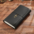 Trifold black leather notebook with brass sword charm on rustic wooden desk