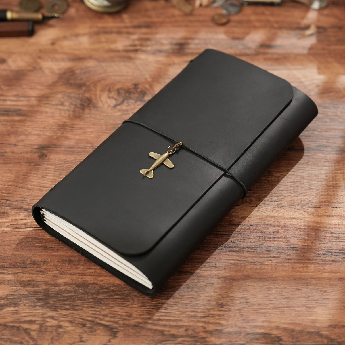 Trifold black leather notebook with brass sword charm on rustic wooden desk