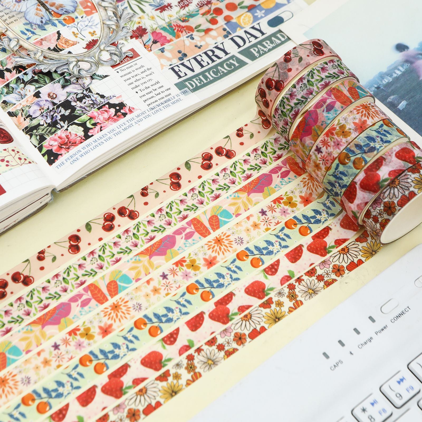A close-up of unrolled Summer Flowers washi tape strips revealing detailed botanical, cherry, and strawberry patterns, laid out beautifully next to a decorated bullet journal.