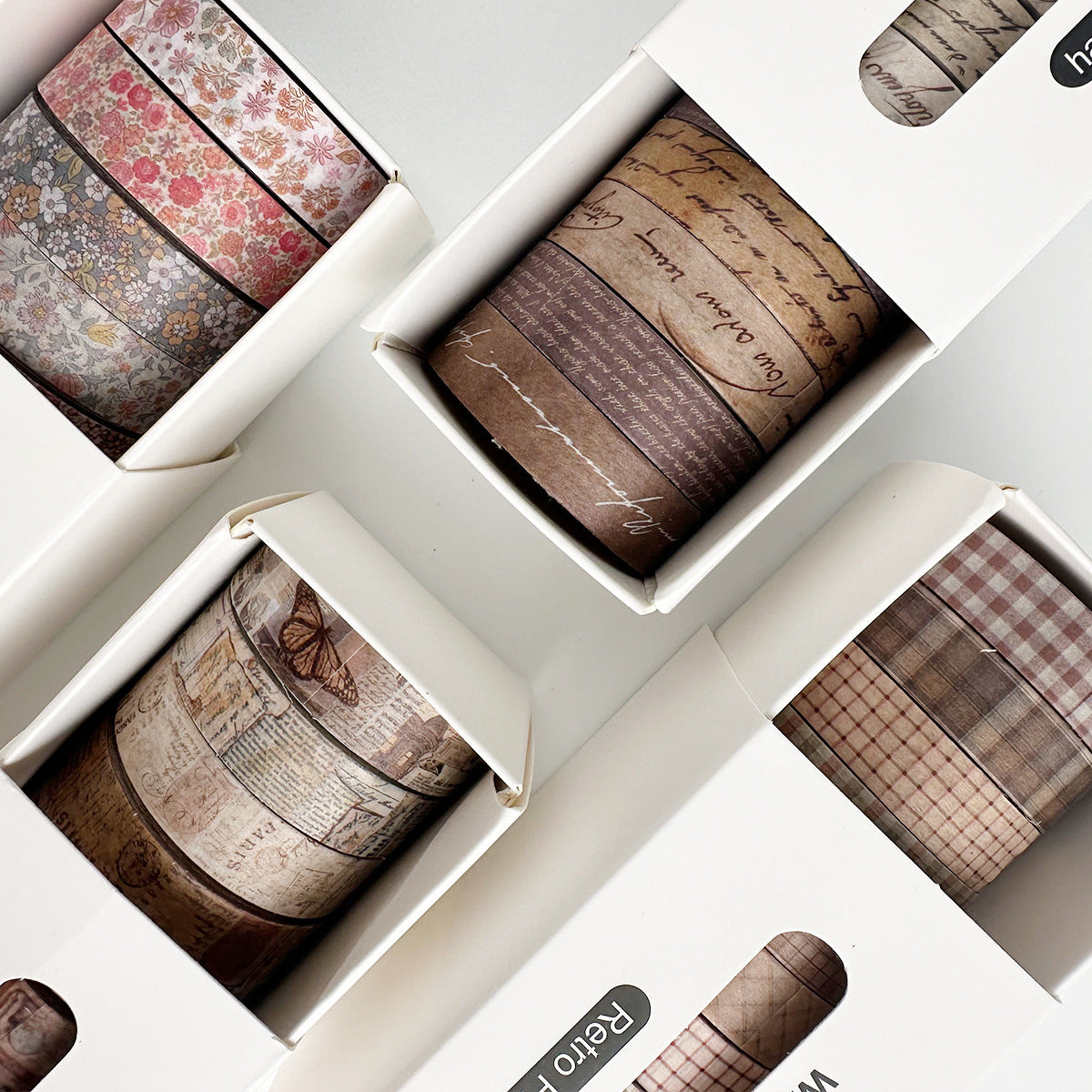 Top-down view of the vintage aesthetic slim washi tape collection in white boxes, displaying the Antique Script, Retro Archives, Faded Blossoms, and Classic Tartan sets ready for junk journaling.
