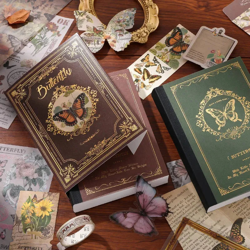 Close-up of the premium A6 hardcover notebooks from the vintage butterfly journal kit. Shows the Nature's Whispers brown cover with an intricate gold foil frame and the Emerald Forest green cover, beautifully displayed with translucent butterfly stickers.