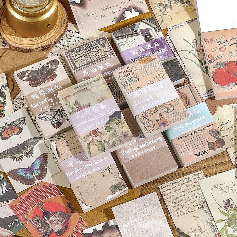 Eight vintage ephemera paper packs with butterfly, floral, map, and newspaper themes on cork board