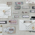 A detailed display of faux-fabric scrap stickers applied to a vintage envelope and textured papers, paired with real wooden buttons to showcase authentic junk journal layering aesthetics.