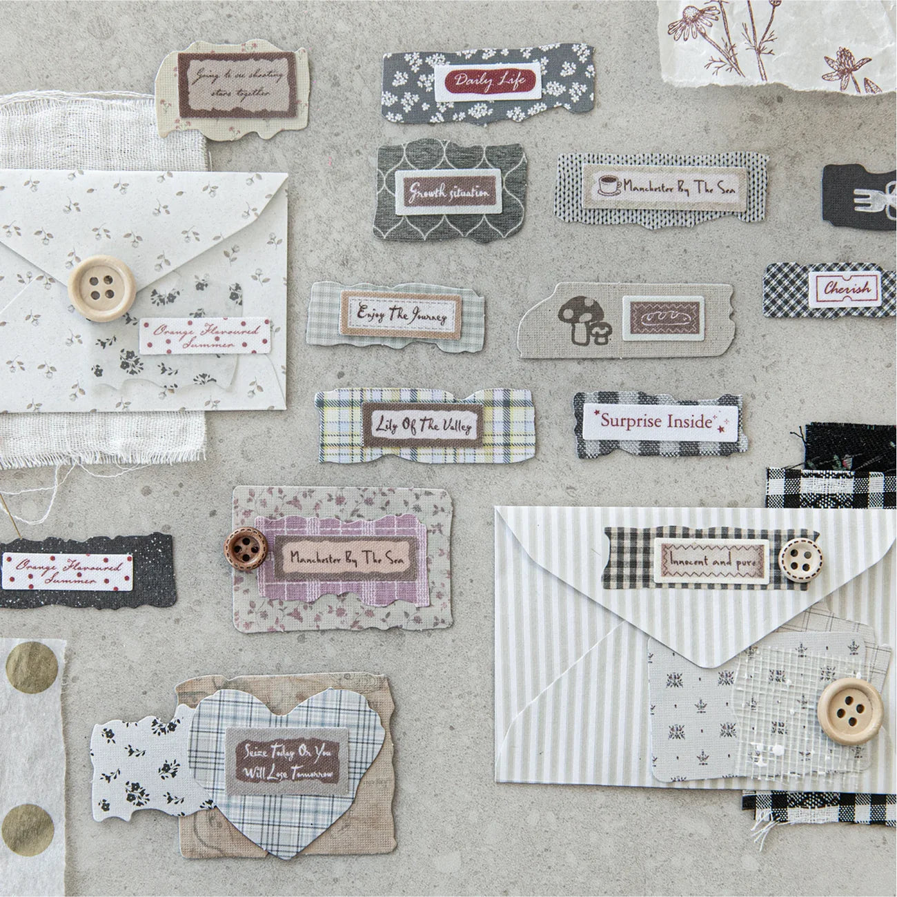 A detailed display of faux-fabric scrap stickers applied to a vintage envelope and textured papers, paired with real wooden buttons to showcase authentic junk journal layering aesthetics.