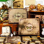 The Nightingale's Love Poems vintage junk journal kit displayed in its antique-style gift box featuring a classic butterfly illustration. Styled with dried roses, a gold mirror, and scattered dark academia ephemera.