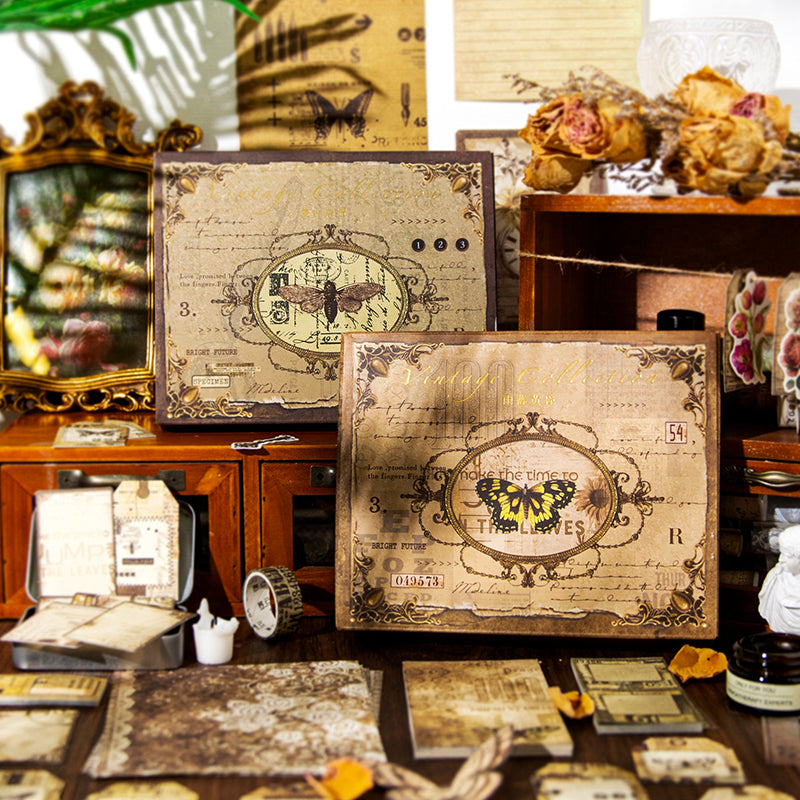 The Nightingale's Love Poems vintage junk journal kit displayed in its antique-style gift box featuring a classic butterfly illustration. Styled with dried roses, a gold mirror, and scattered dark academia ephemera.