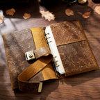 Top-down view of the Embossed Antique Floral leather journal lying completely open on a rustic wooden desk. Showcases the raw suede interior of the top-grain cowhide, the vintage metal lock strap, and the binder mechanism.