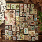 All 50 angel postage stamp stickers laid out with a vintage rose postcard – cherub designs in soft pink and sepia tones
