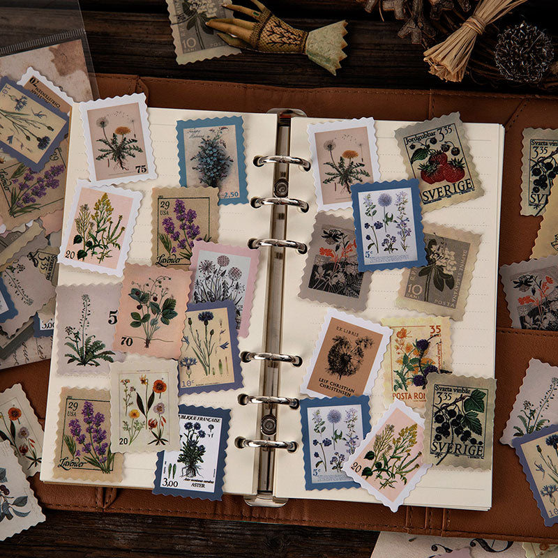 Botanical vintage postage stamp stickers on brown leather journal pages, lavender and wildflower illustrations with serrated edges.