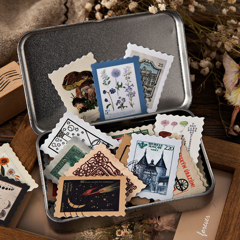 Vintage postage stamp stickers stored in a small metal tin, showing mushroom castle and space rocket illustrations with serrated edges.
