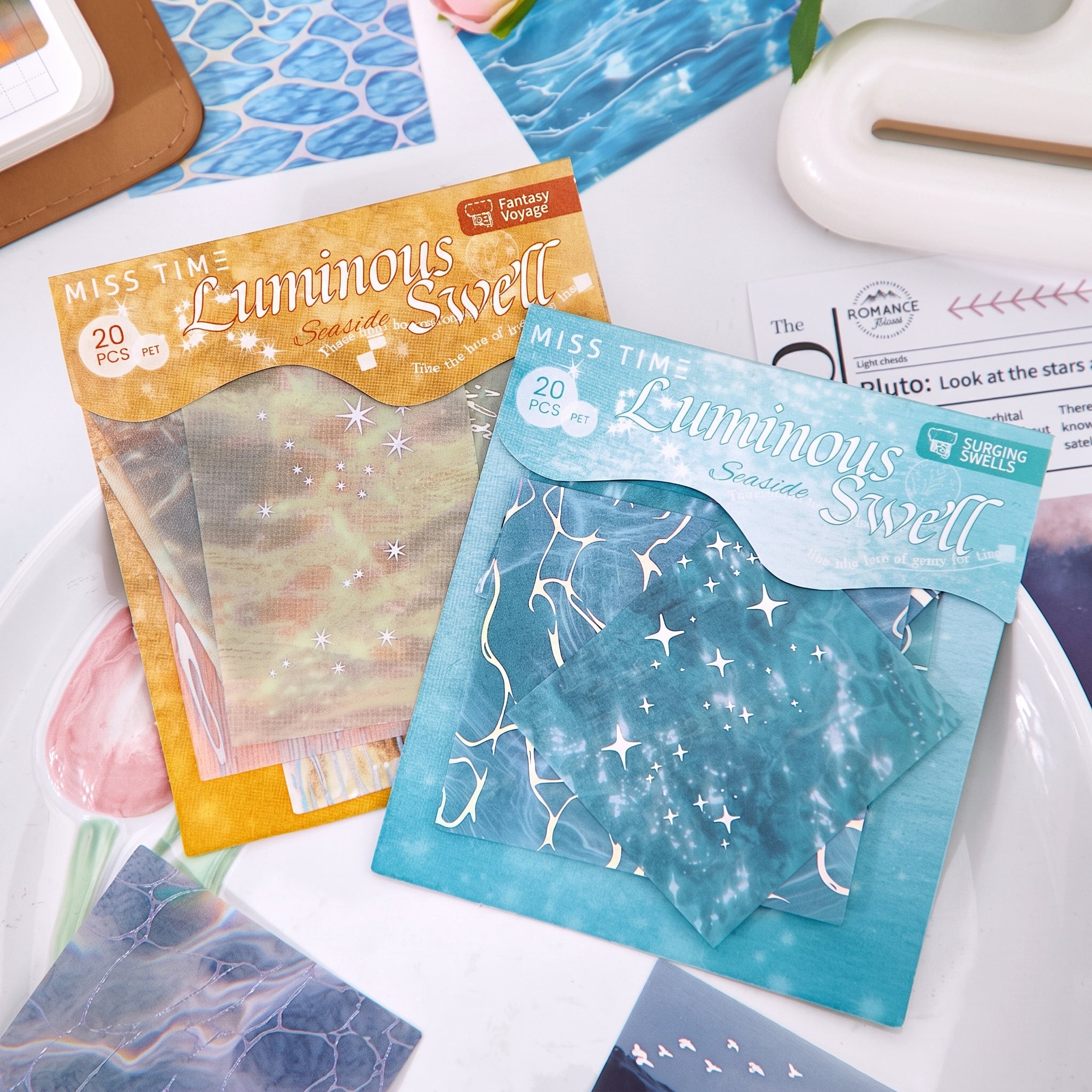Two Luminous Swell water ripple sticker packs in gold and teal on white desk with journal supplies